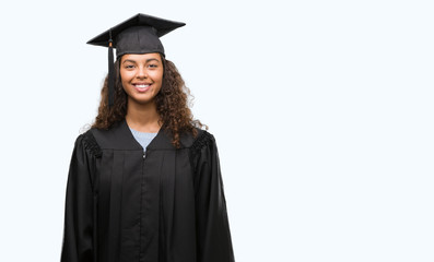 Young hispanic woman wearing graduation uniform with a happy face standing and smiling with a...