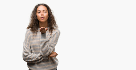 Beautiful young hispanic woman wearing stripes sweater looking at the camera blowing a kiss with hand on air being lovely and sexy. Love expression.