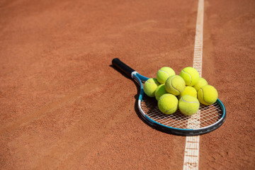 Close-up of racket with many balls lying on sunny court. Equipment is being used for sport contest on lovely day. Copy space in left side