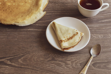 a pancake in a plate, coffee and a teaspoon lying on a wooden table in a rustic style