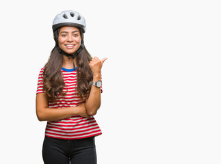 Young arab cyclist woman wearing safety helmet over isolated background smiling with happy face looking and pointing to the side with thumb up.