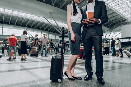 Stay here. Full length portrait of adult man and woman are waiting for their flight, while holding passport with tickets