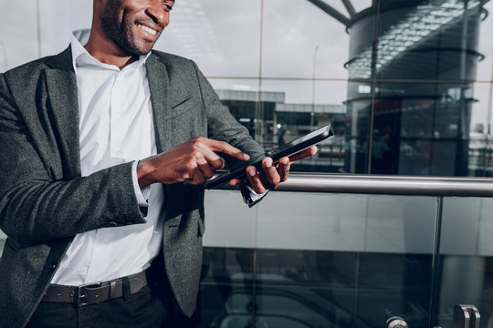 Sending messages. Close up of male hands typing message on gadget. Man is standing at glass fence outside the airport. Copy space in right side
