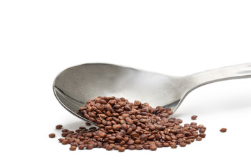 Close up of tilted metal spoon with red quinoa seeds isolated on white background