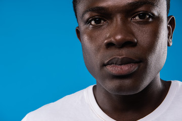 Kind face. Close up portrait of handsome male in white t-shirt. Isolated on blue background. Copy space in left side