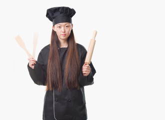 Young Chinese woman over isolated background wearing chef uniform with a confident expression on smart face thinking serious