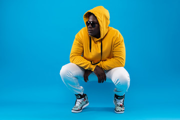 My style. Studio portrait of young man in yellow hoodie hunkering down and looking away with calm...