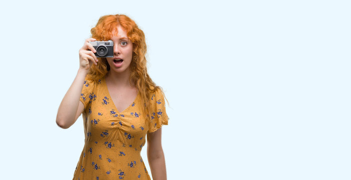 Young redhead woman taking pictures holding vintage camera scared in shock with a surprise face, afraid and excited with fear expression