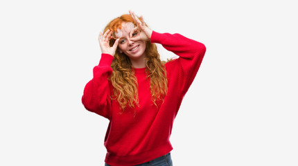 Young redhead woman wearing red sweater doing ok gesture with hand smiling, eye looking through fingers with happy face.