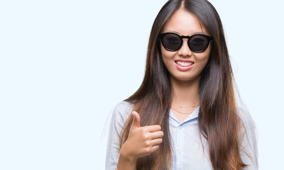 Fototapeta premium Young asian woman wearing sunglasses over isolated background doing happy thumbs up gesture with hand. Approving expression looking at the camera with showing success.