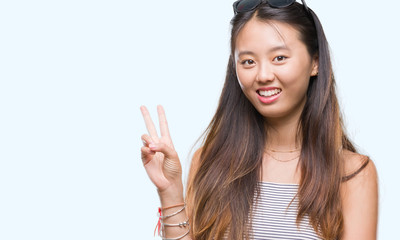 Young asian woman wearing sunglasses over isolated background smiling with happy face winking at the camera doing victory sign. Number two.