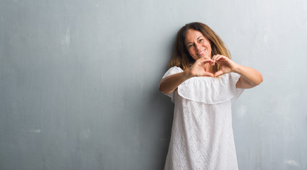 Fototapeta na wymiar Middle age hispanic woman standing over grey grunge wall smiling in love showing heart symbol and shape with hands. Romantic concept.