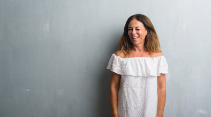 Fototapeta premium Middle age hispanic woman standing over grey grunge wall winking looking at the camera with sexy expression, cheerful and happy face.