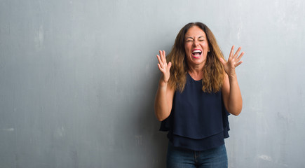 Middle age hispanic woman standing over grey grunge wall celebrating mad and crazy for success with...