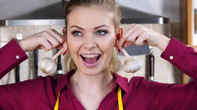 Cheerful woman having fun pretending garlic is her earrings. Healthy vegetable, dieting food concept