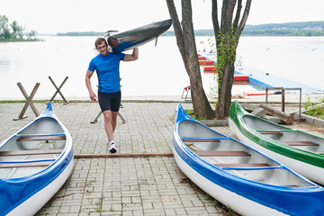 Young sportsman carrying his kayak after rowing competition outdoors