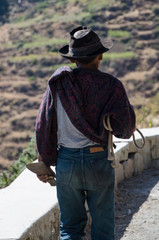 Close-up of old farmer with hat walking with a knife at the edge of the cliff by a mountain