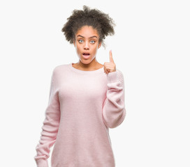 Young afro american woman wearing winter sweater over isolated background pointing finger up with successful idea. Exited and happy. Number one.