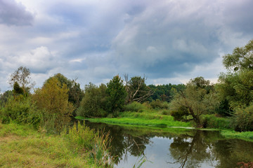Fototapeta na wymiar River landscape on a background of dramatic gray sky with clouds in autumn day