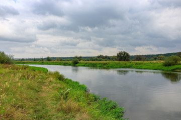 Fototapeta na wymiar View of river surface on a background of sky with gray clouds. River landscape on a autumn day
