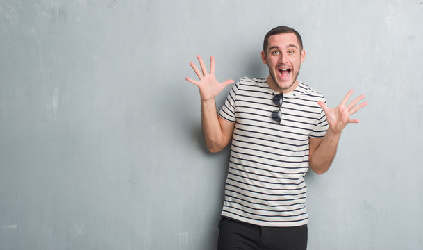 Young caucasian man over grey grunge wall celebrating crazy and amazed for success with arms raised and open eyes screaming excited. Winner concept