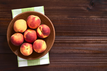 Fresh ripe peaches on clay plate, photographed overhead on dark wood with natural light
