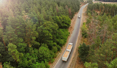 Aerial. Grain carrier trucks on a country road between the forest.