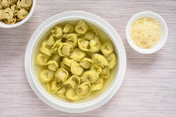 Italienische traditionelle Tortellini in Brodo (Brühe) Suppe mit geriebenem Käse an der Seite, fotografiert mit natürlichem Licht
