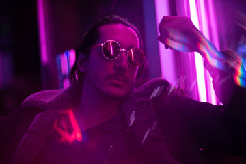 Long hair girl with sunglasses and leather jacket looking at neon lights