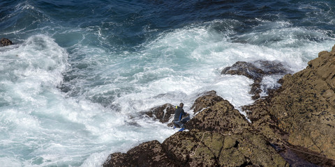 unidentified Barnacles Fisherman in wetsuit at his dangerous work farming Goose Barnacles on the cliffs of cape tourinan, coast of death (costa da morte),galizia, spain