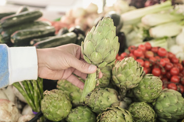 Artichokes. Close up on choosing picking up tasty artichoke, buying seasonal ingredient fresh natural background. Healthy nutrition lifestyle choice, traditional local season marketplace closeup image