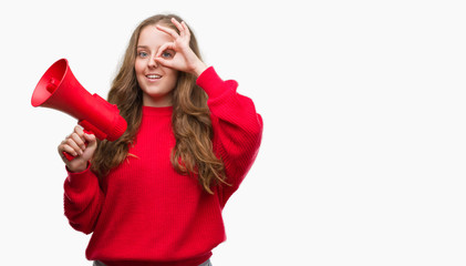 Naklejka premium Young blonde woman holding red megaphone with happy face smiling doing ok sign with hand on eye looking through fingers