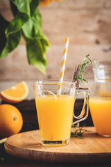 Glass of fresh pressed orange juice and oranges on wooden table. Autumn cozy rustic mood still life