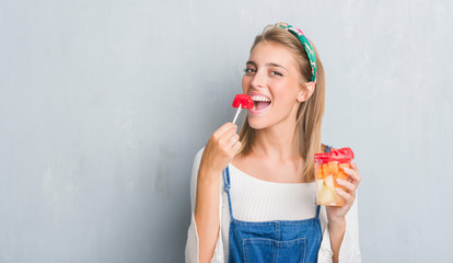 Beautiful young woman over grunge grey wall eating fruits with a confident expression on smart face...