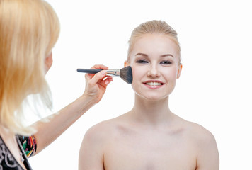 Fototapeta premium Hand of makeup master applying powder for young woman model on white background. Professional make up applying by artist. Beautiful girl face with perfect skin. Make-up detail in process