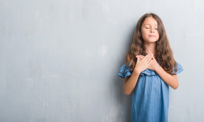 Fototapeta premium Young hispanic kid over grunge grey wall smiling with hands on chest with closed eyes and grateful gesture on face. Health concept.