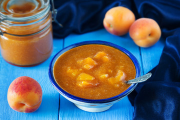 Apricot jam with spoon and fruit on blue table