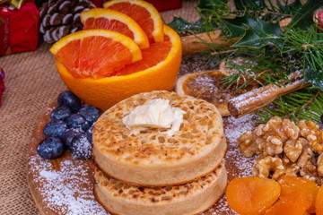 Toasted Crumpets with Butter.  Warm toasted Crumpets with Butter on a chopping board with a selection of dried fruit and nuts. Surrounded by Christmas presents and gifts.