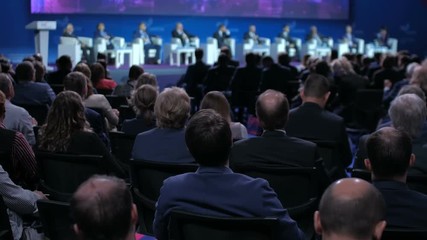 Audience in a conference hall listening to the speakers presentation on the stage.