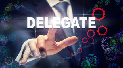 A businessman pressing a Delegate business concept on a graphical display of cogs