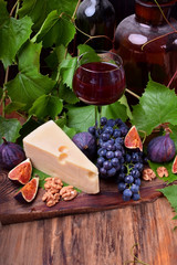 Red wine in a glass surrounded by the snacks: Maasdam cheese, figs, walnuts and a bunch of Isabella grapes on a wooden board