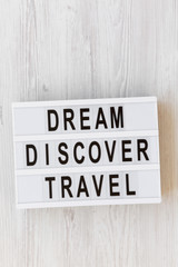 Modern board with text 'Dream Discover Travel' word on white wooden surface, overhead view. From above, flat lay, top view.