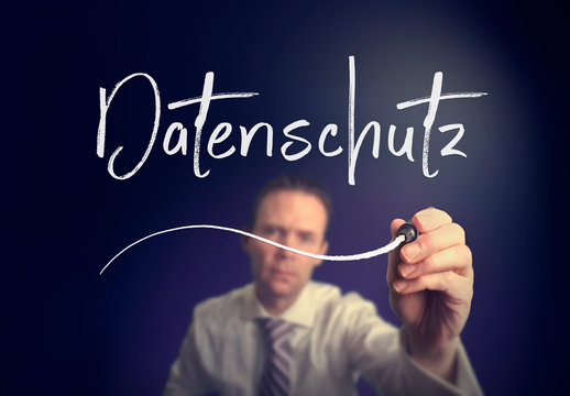 A businessman writing a  Data Protection "Datenschutz" concept in German with a white pen on a clear screen.