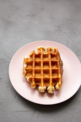 Traditional belgian waffle on pink plate over concrete background, high angle view.