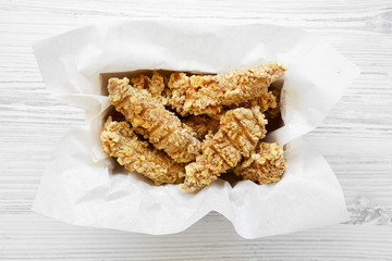 Chicken strips in paper box on a white wooden table, overhead. Flat lay, from above, top view. Close-up.