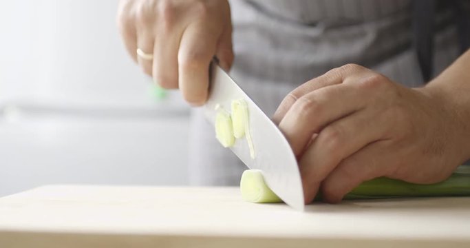 Slow motion close up shot of cook finely chop leeks on wooden Board