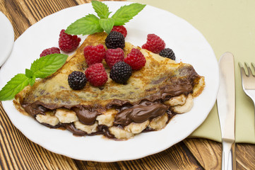 Homemade crepes served with chocolate cream, fresh blueberries and raspberries, powdered sugar on a white background