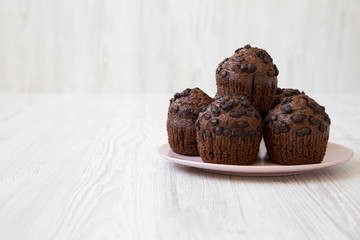 Chocolate cupcakes on pink plate on white wooden background, low angle view. Space for text.