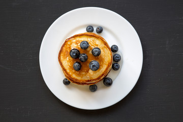 Pancakes with blueberries and honey on white plate on dark wooden background, top view. Flat lay, overhead, from above.