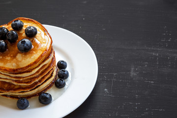 Pancakes with blueberries and honey over black background, side view. Copy space.